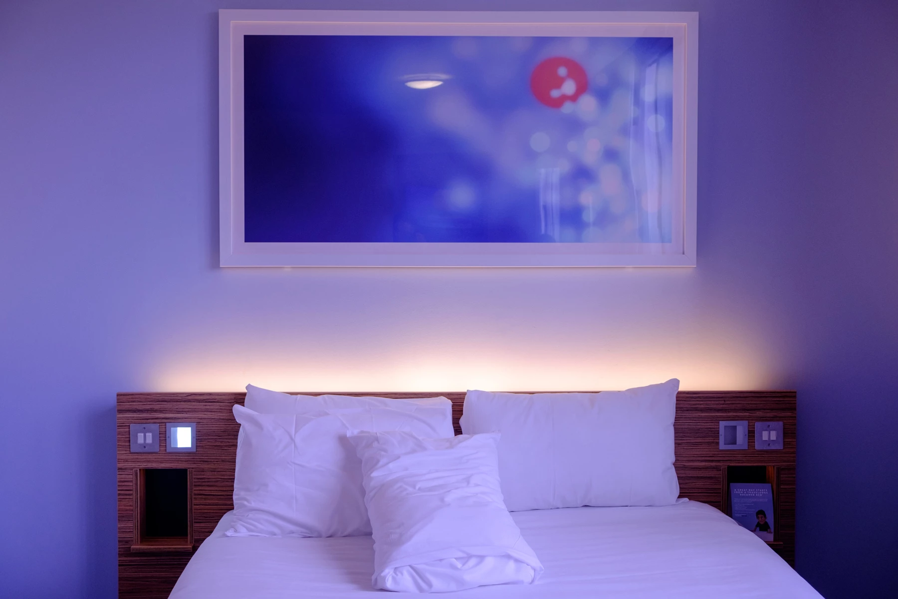 A hotel bed in a room with relaxing mood lighting set
