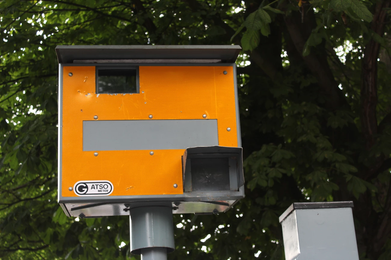 A yellow speed camera placed high above a road in-front of a tree