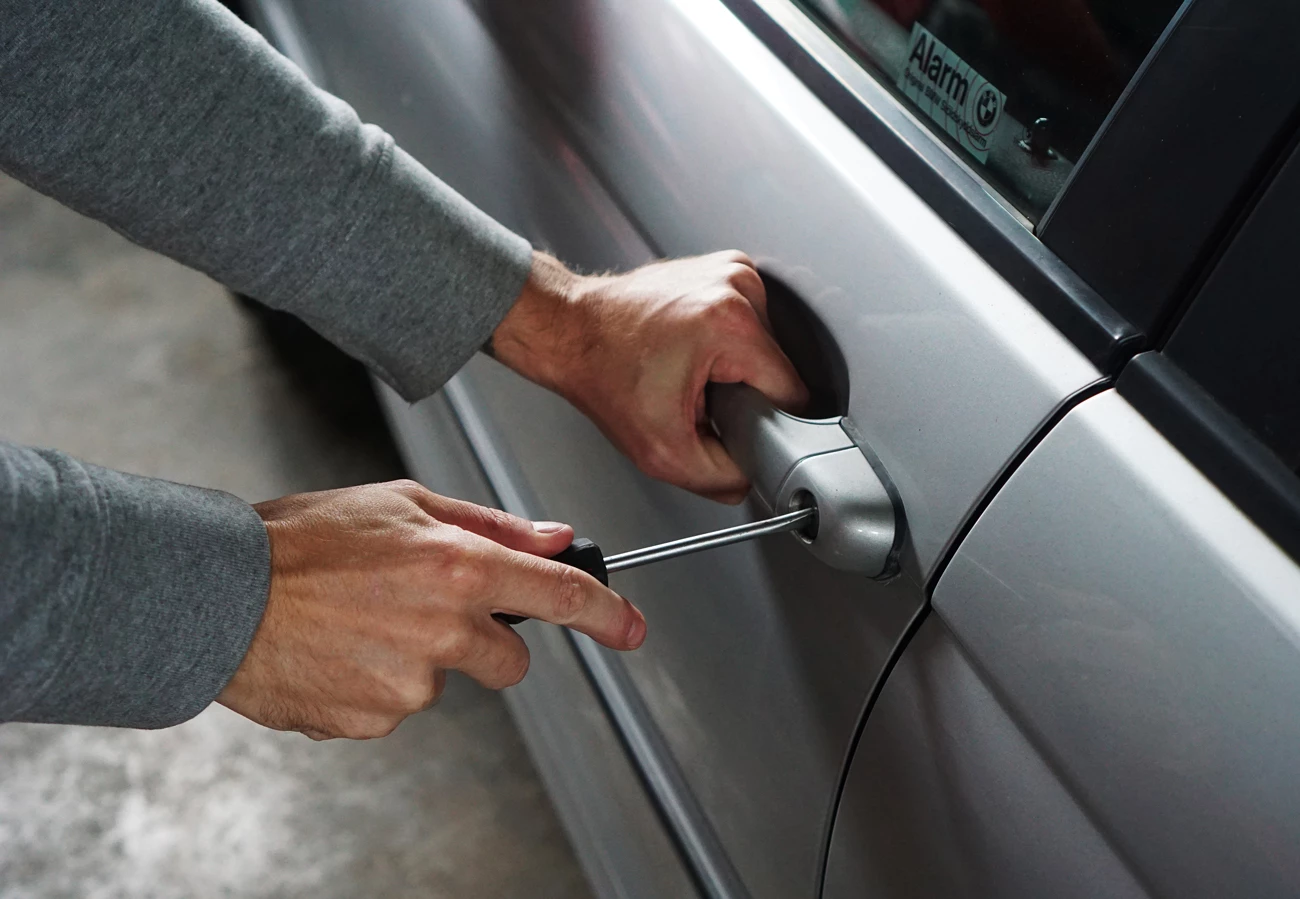 A car thief using a screwdriver to break into a car on a forecourt