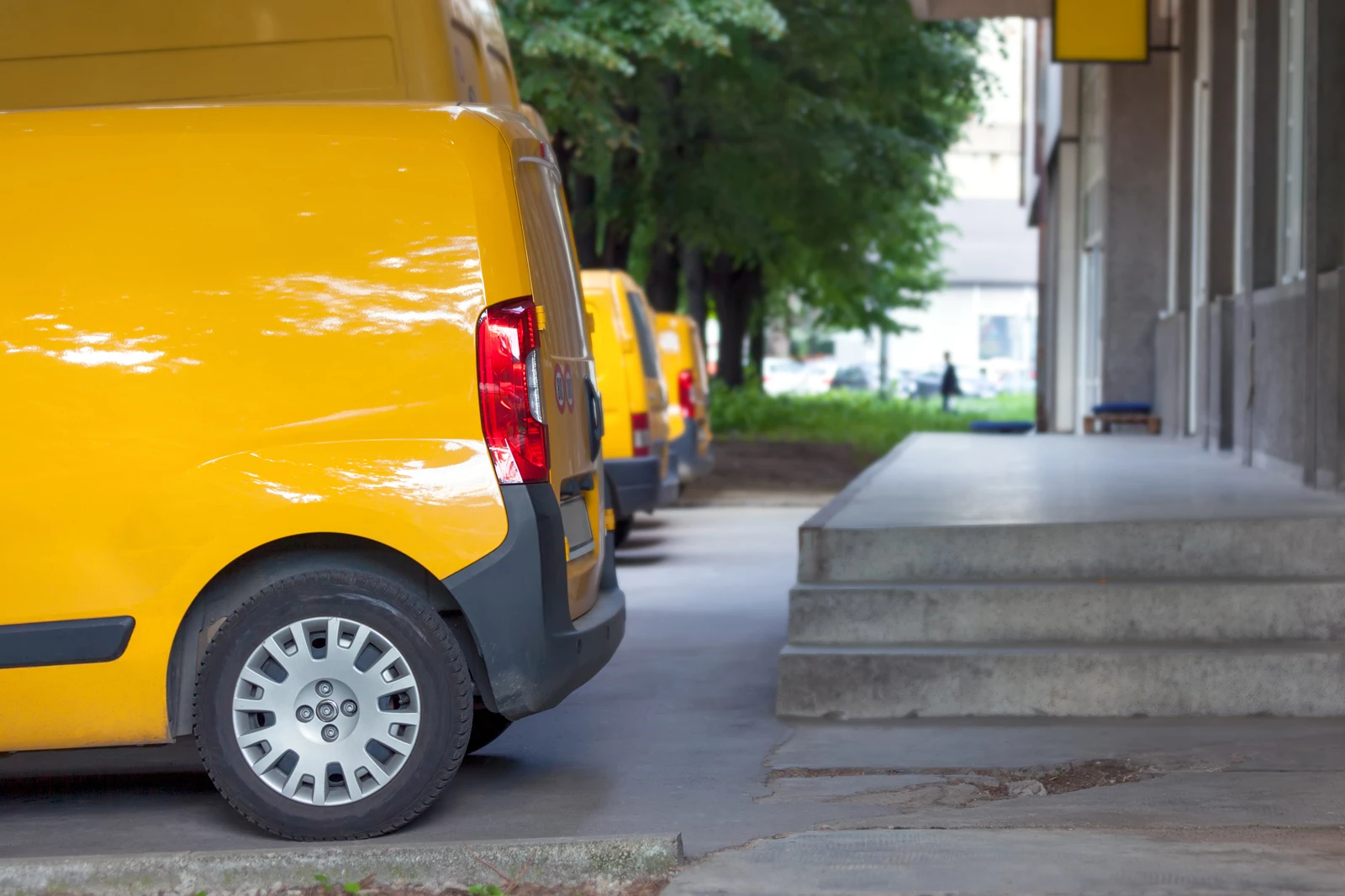 Three yellow vans parked in a row outside a businesses depot