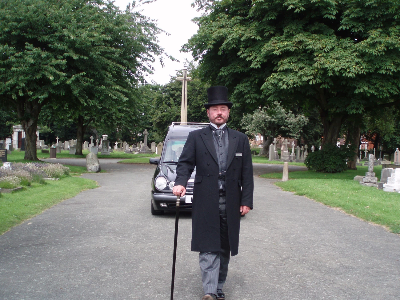 A funeral director walking in-front of a hearse