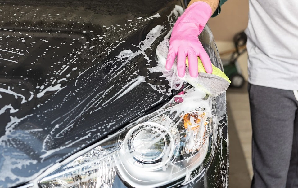A car valeter cleaning the front of a car covered in soap