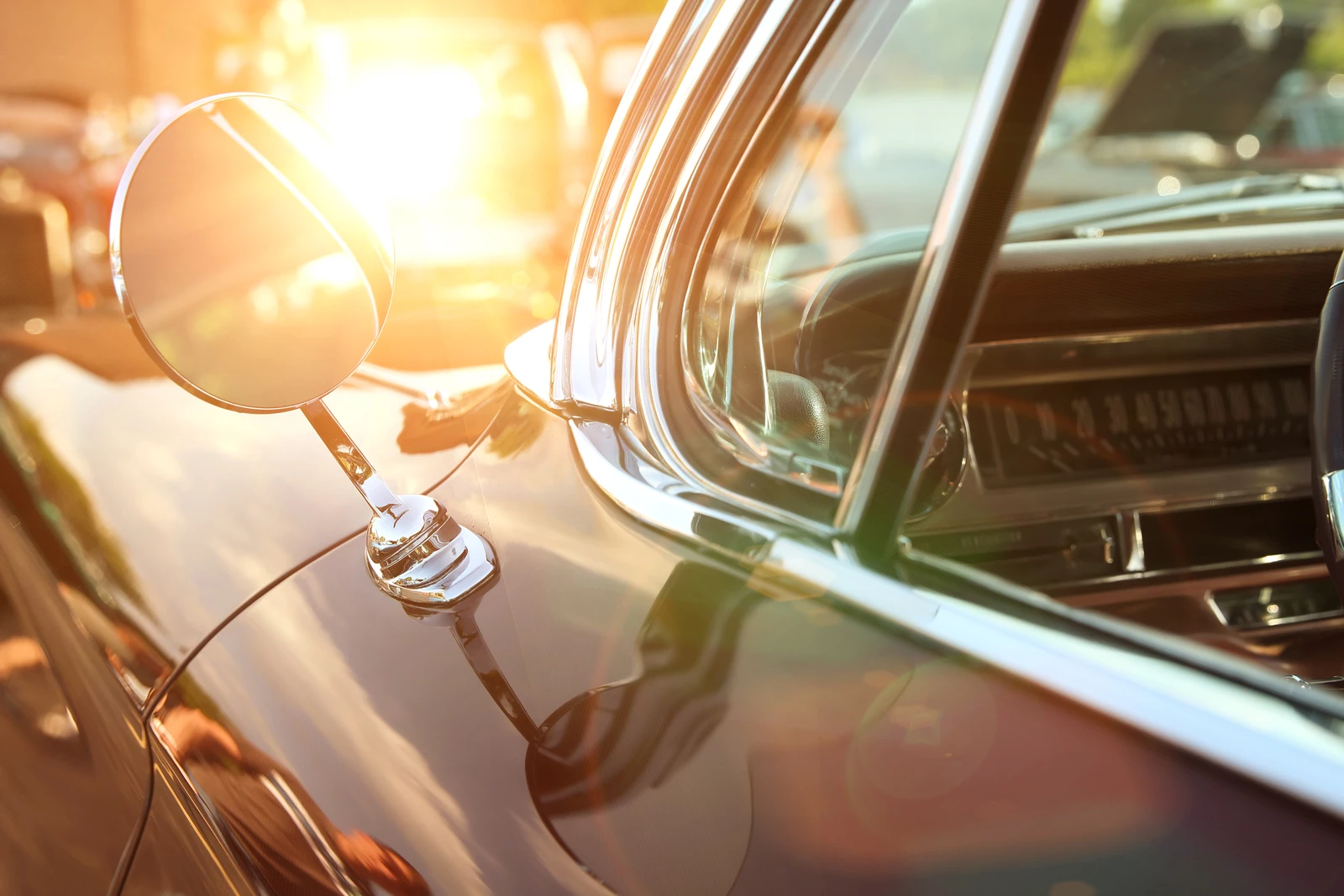 The front corner of a classic 1960's car with the sun setting behind it