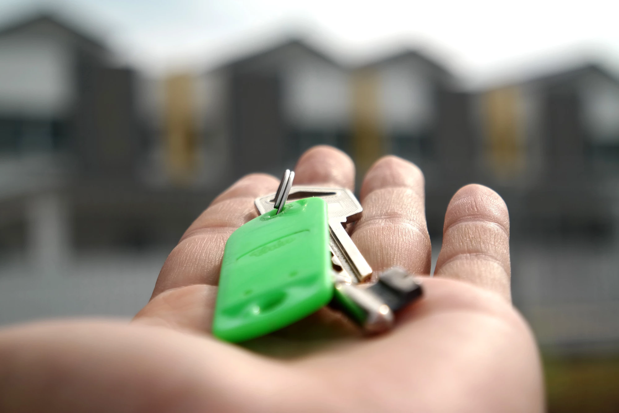 A person holding a key out on their hand with blurred out houses in the background