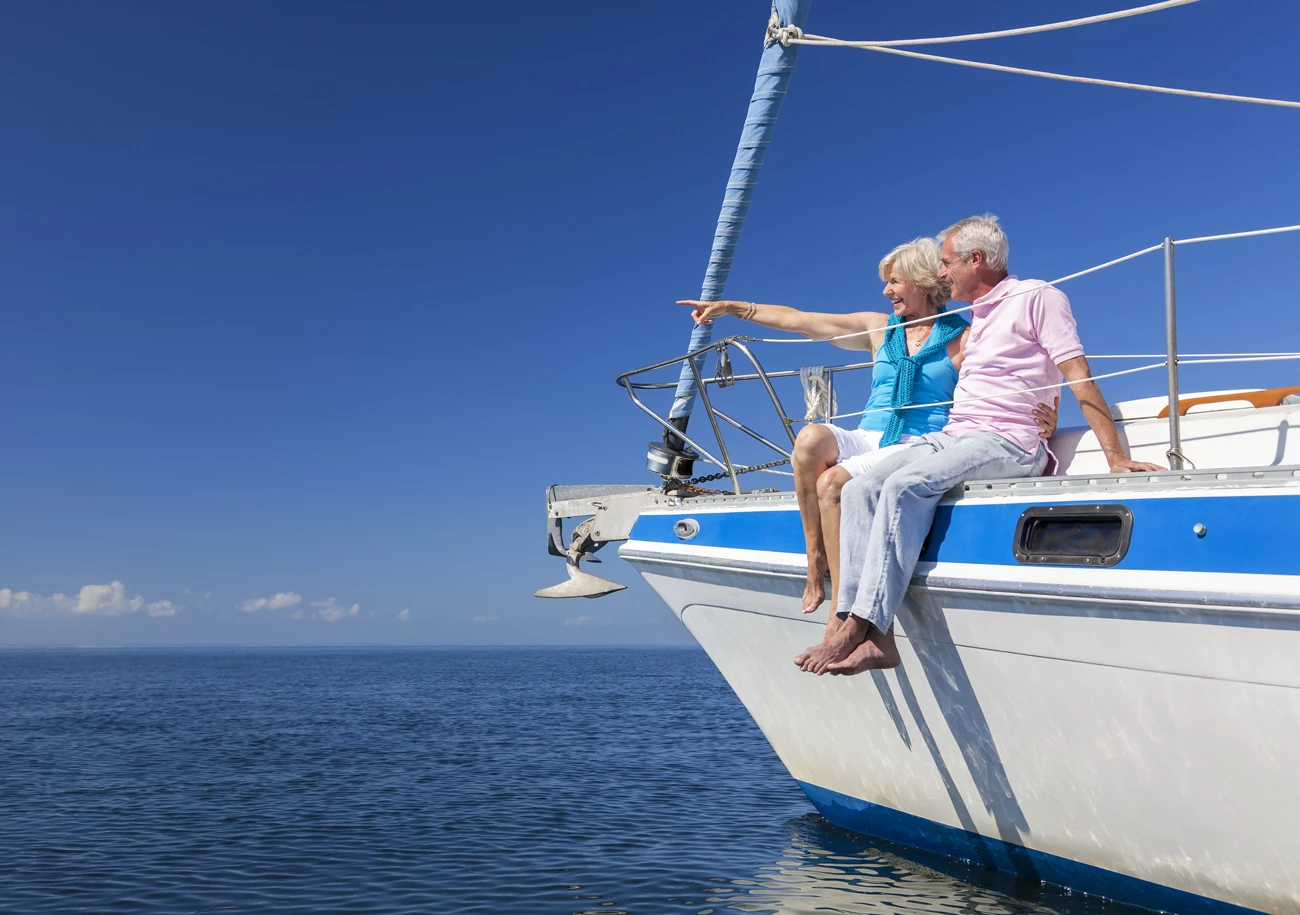 A older couple sitting on the side of a sailing boat smiling at sea