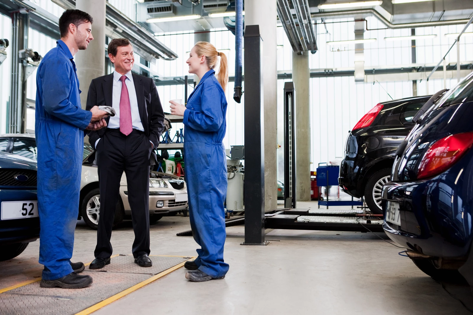Two training MOT testers standing with the business owner in a busy garage workshop