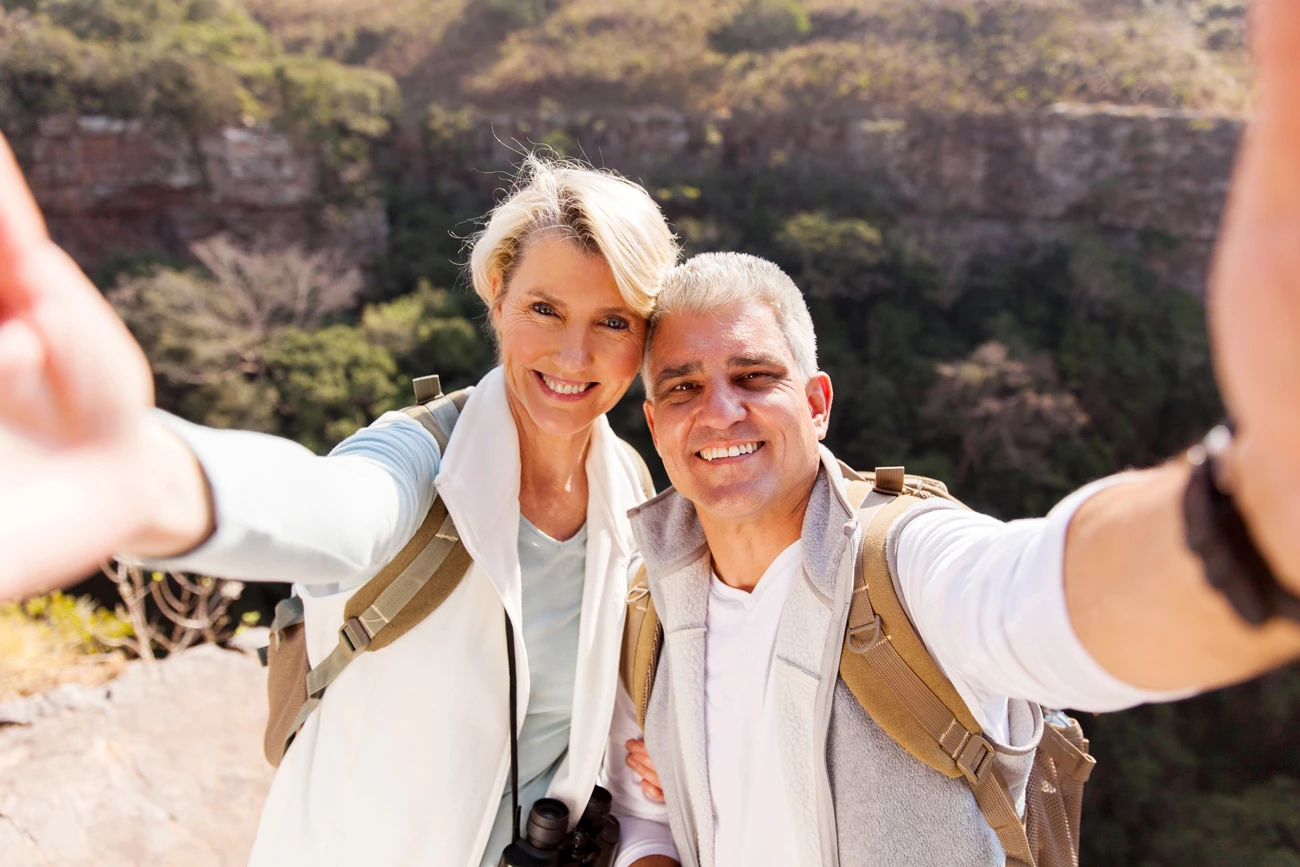 Middle aged couple taking a holiday selfie together in front of scenic view filled with greenery