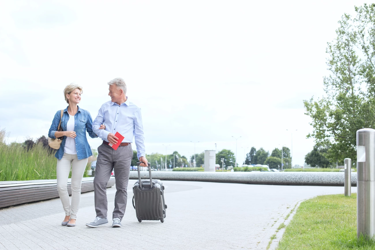 Middle aged couple walking to airport with suitcase