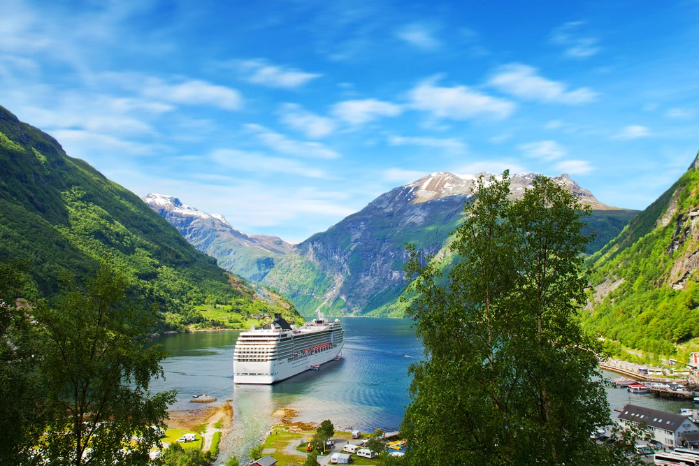 A cruise ship setting off on a body of water in a valley surrounded by mountains