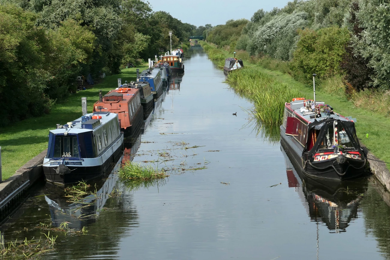 A canal with canal boats docked on the side stretching across a country area