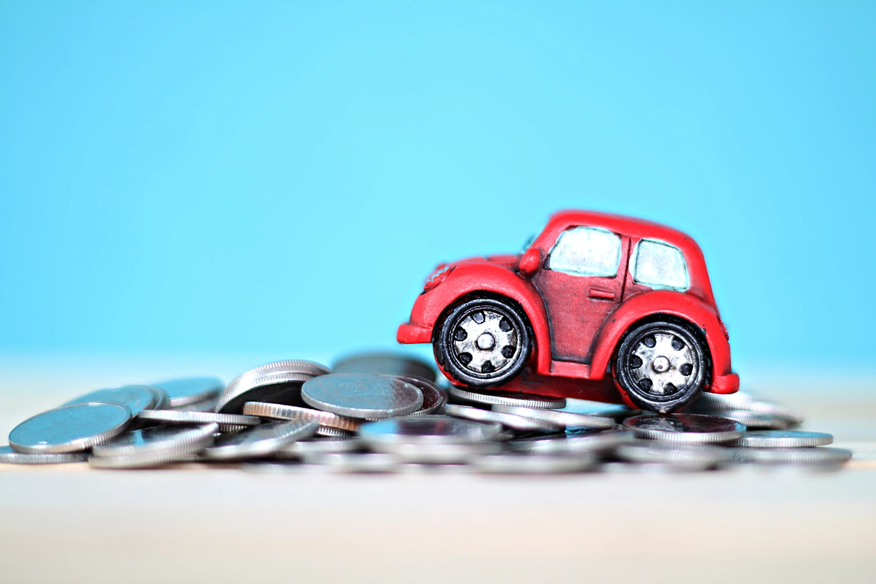 A model car on a pile of silver coins against a plain blue background