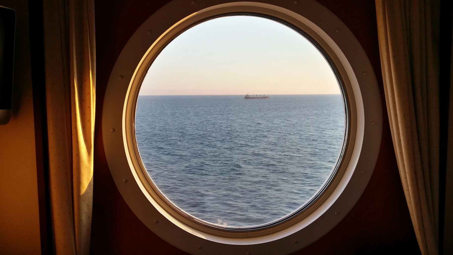 A view of the ocean from a round cruise ship cabin window at sunset