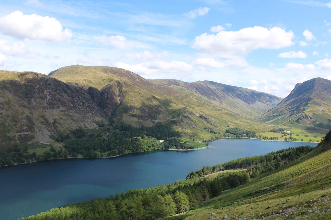 A long blue lake sitting between rolling green hills in the Lake District