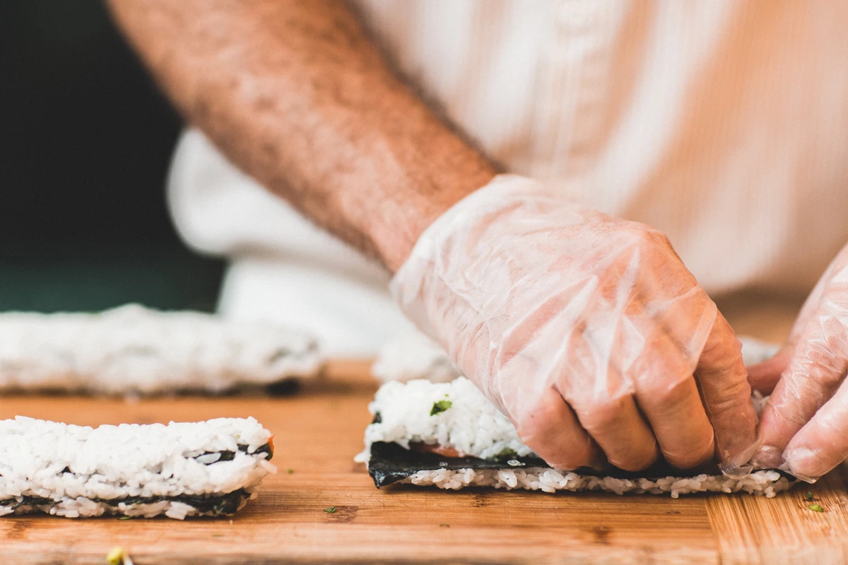 A chef wearing gloves rolling sushi on a work surface