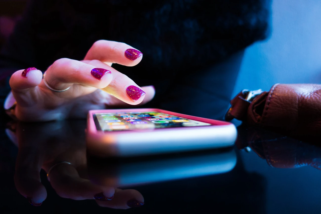 A persons hand uding a mobile phone on a desk