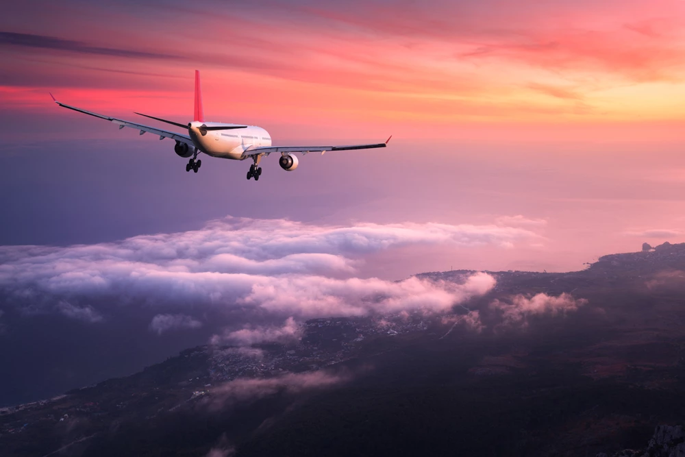 An commercial air liner flying above the clouds with a red sunset in the distance