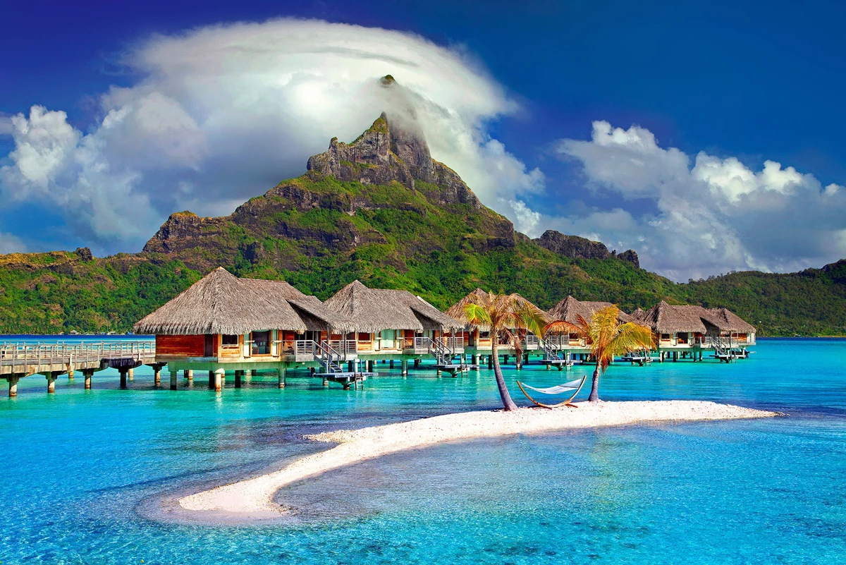 Tropical island of Bora Bora with huts on stilts in the sea and a mountain in the distance on a sunny day