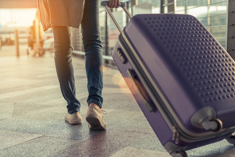 Person walking through airport with suitcase trailing in sunset
