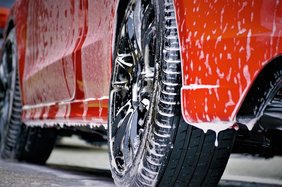 An orange car dripping with shampoo bubbles during a car wash