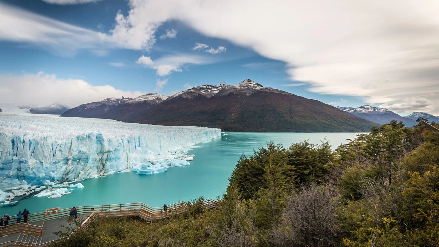 The Perito Moreno Glacier in Argentina with walkways on a near bank, mountains in the distance and a light blue lagoon in-front of the glacier