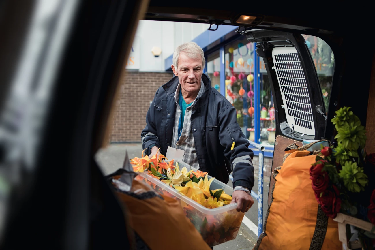 A man unloading flowers in a box from the back of a work van