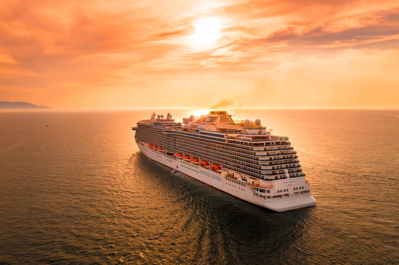 A large cruise ship ship on the sea at sunset with the sky glowing