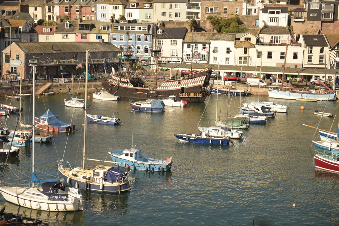 A quaint harbour in Brixham with small boats docked and seafront houses around the harbour