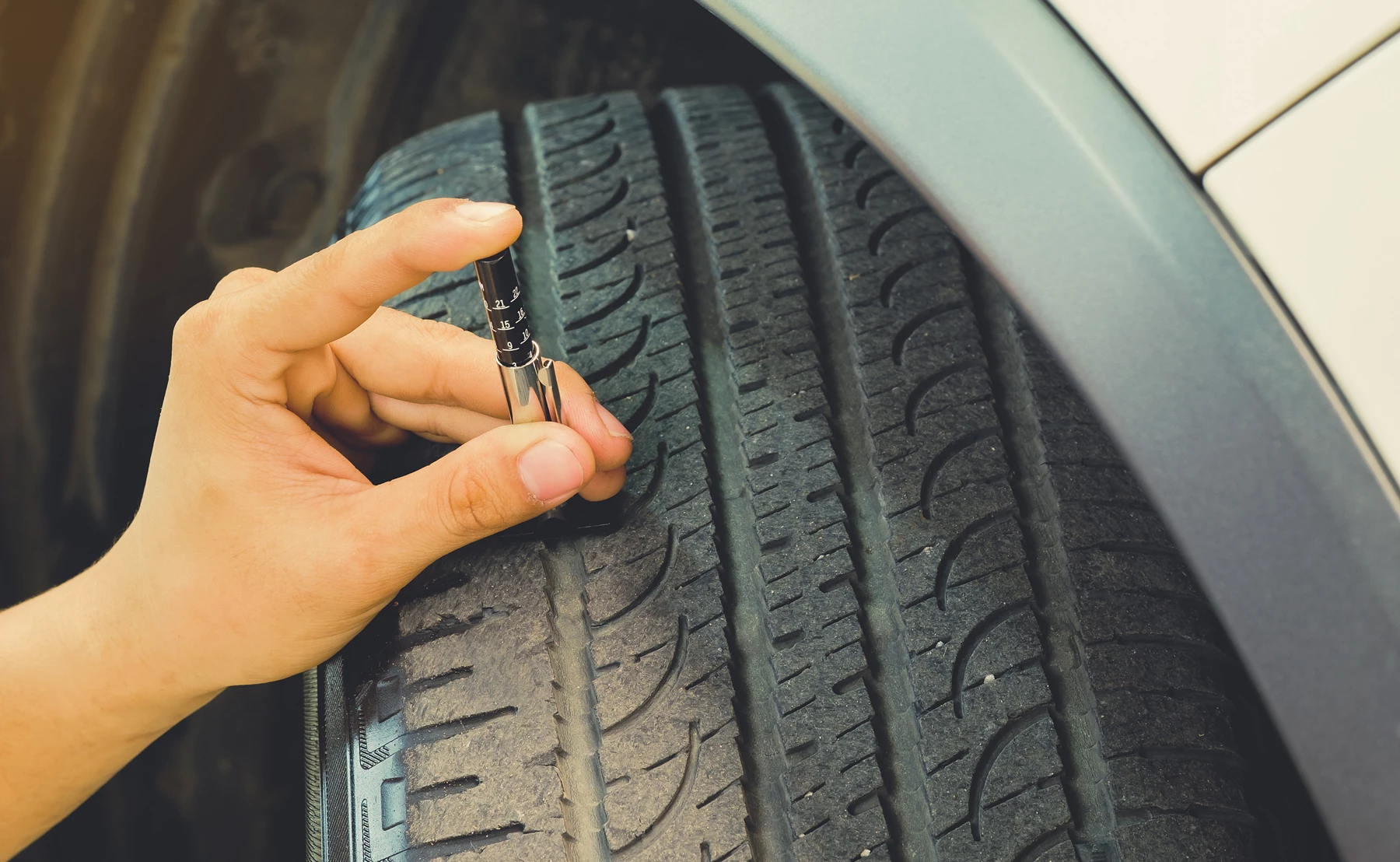 A mechanic using a tool to check the tread depth of a car tyre