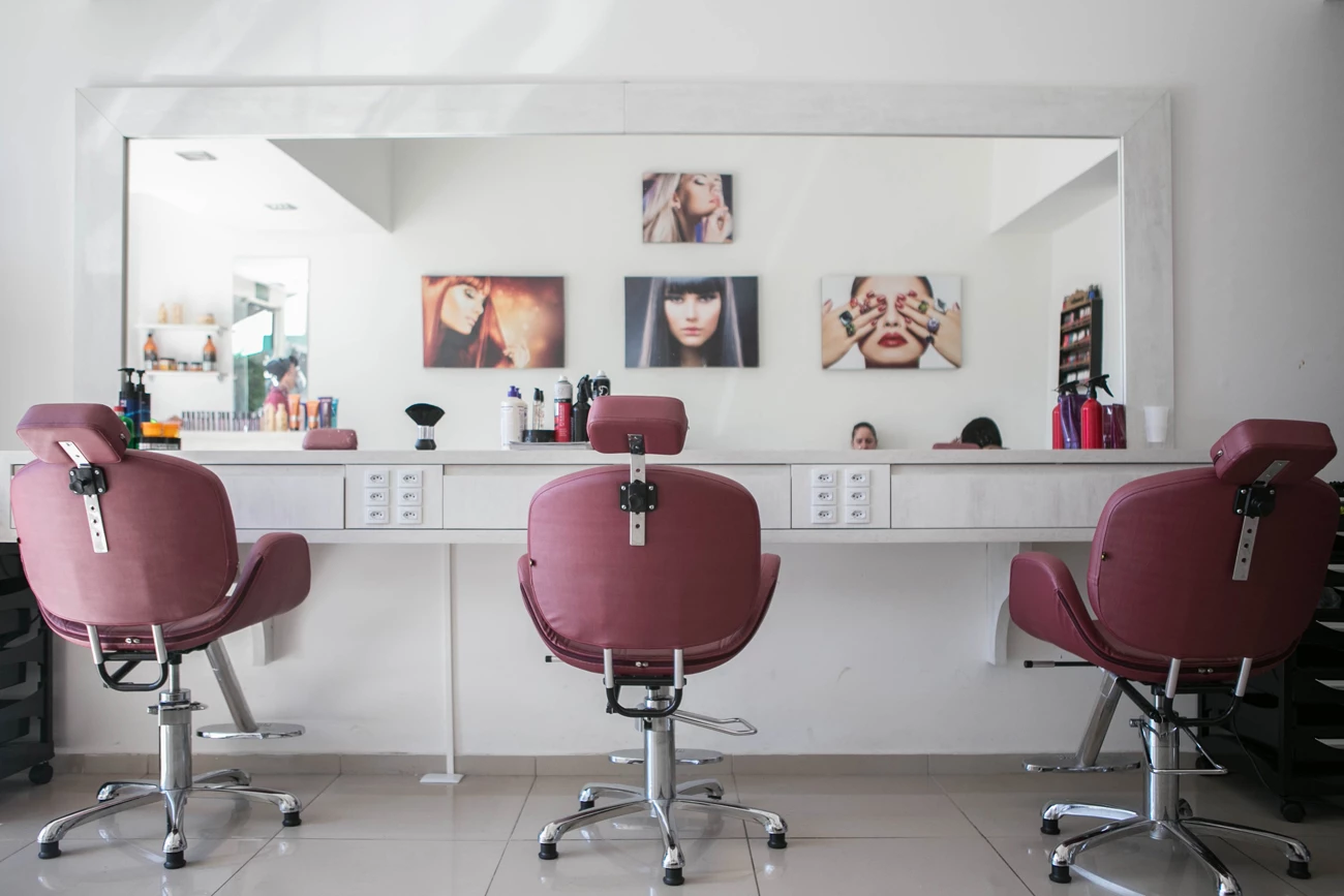 A clean and tidy hair salon with three chairs in-front of a long mirror