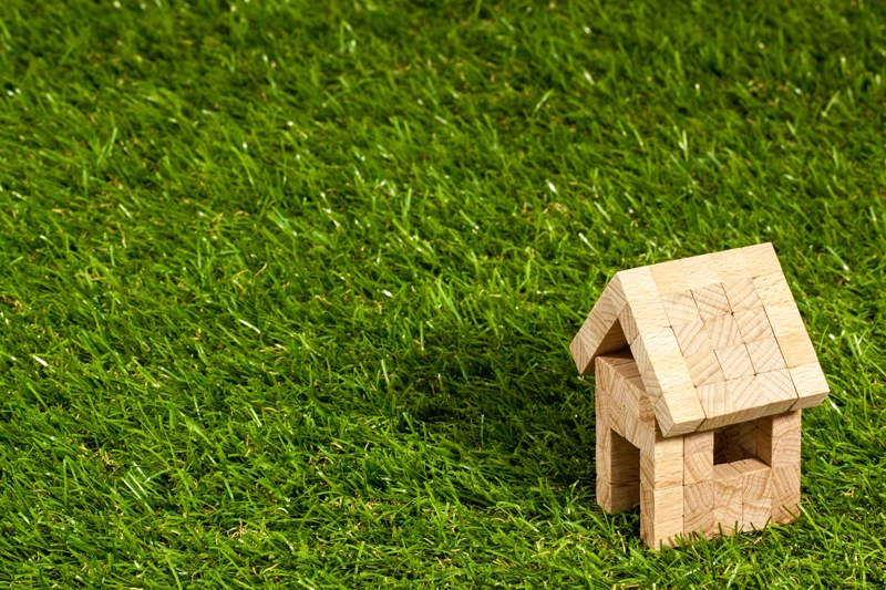 A model house made of wooden blocks on a patch of vibrant green grass