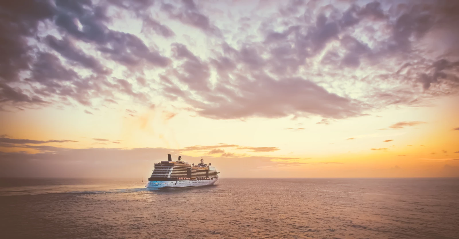 A cruise ship on a large ocean heading off into the sunset
