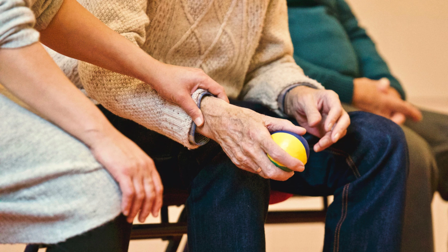 A care worker helping an elderly person exercise their hands with a ball