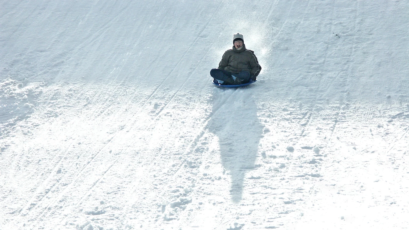 A young boy sledging down a snowy slope