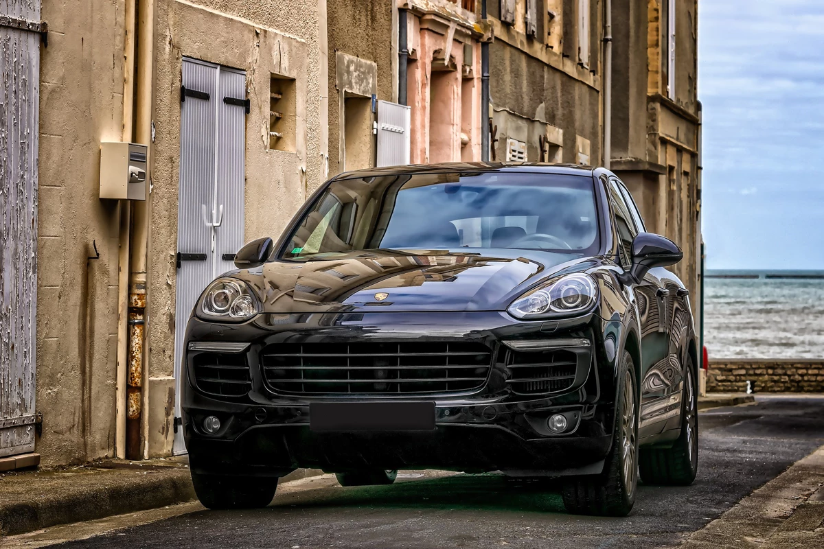 A Porsche SUV driving down a street in a town with the sea in the distance