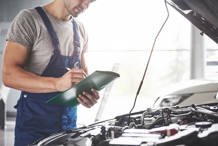 A mechanic writing on a notepad whilst MOTing a vehicle 