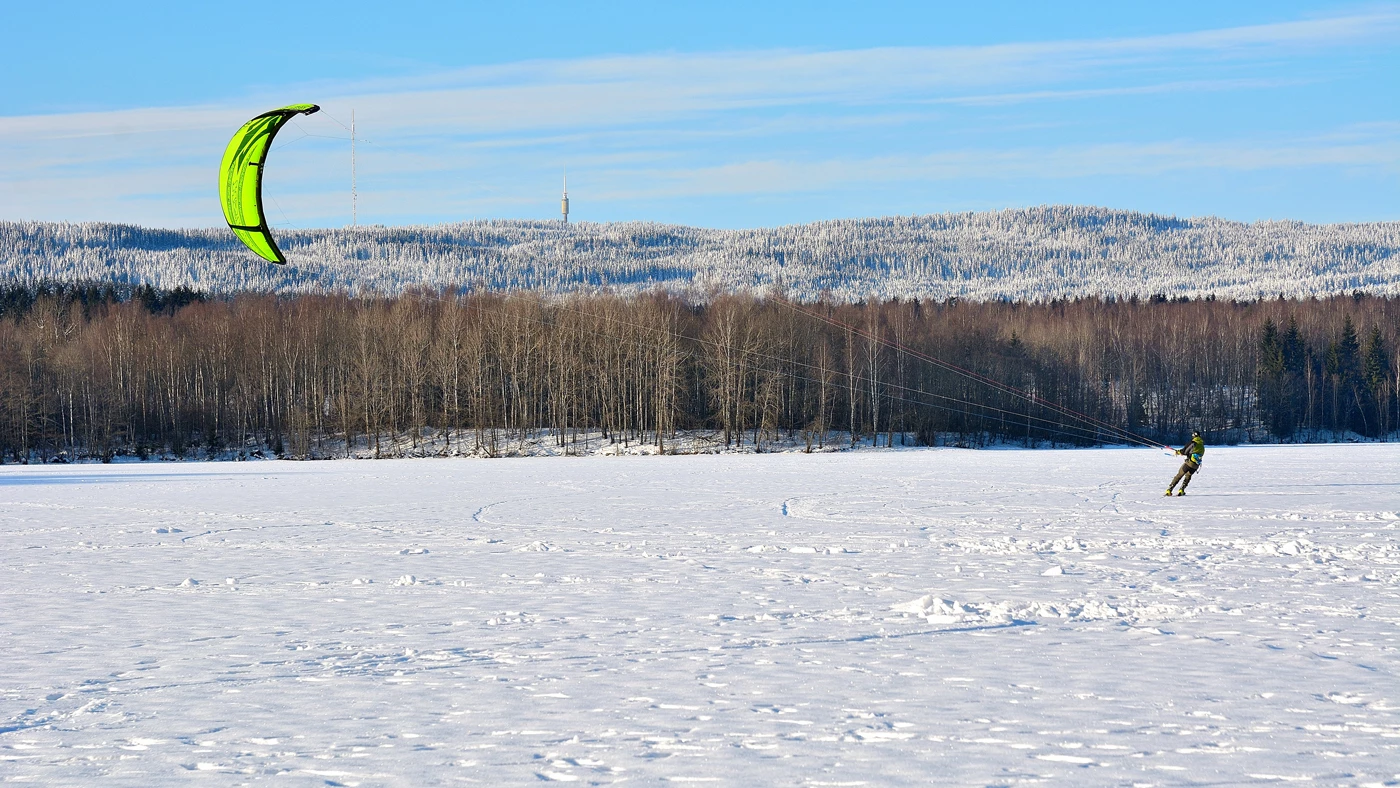 A person snow kiting on a large flat area of snow with woodland in the background