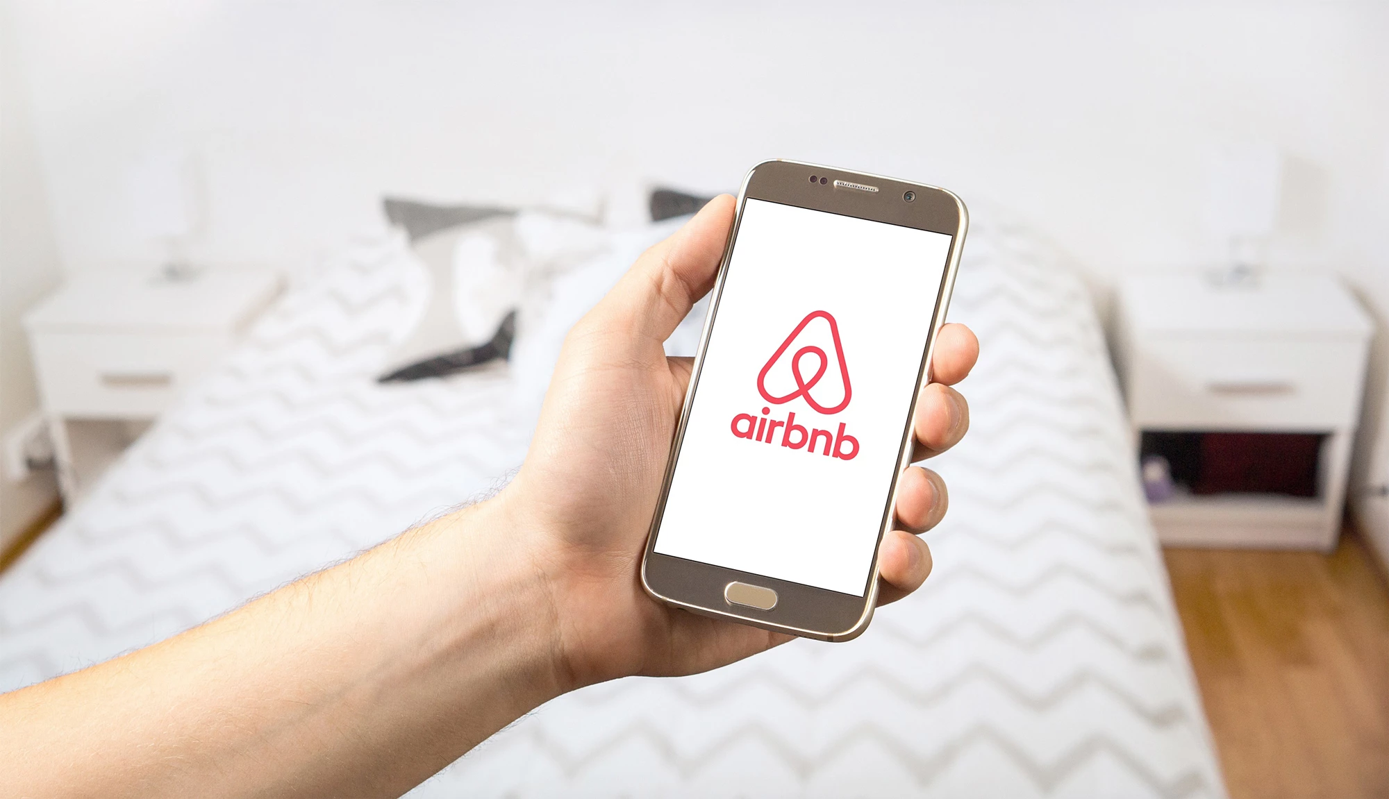 A person holding a phone in front of them with the Airbnb app opening in a bedroom