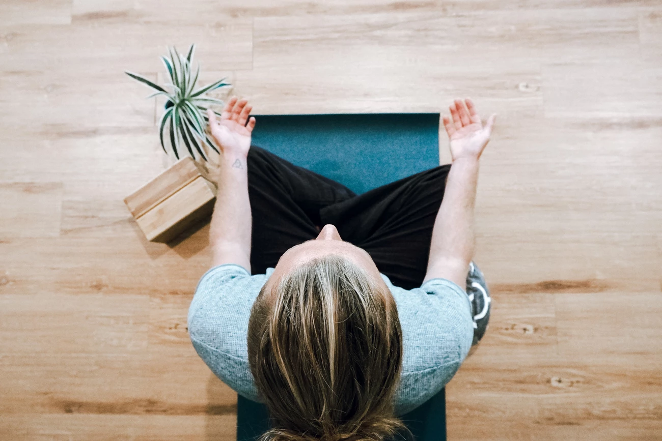 An overhead view of a woman sitting on a wooden floor meditating