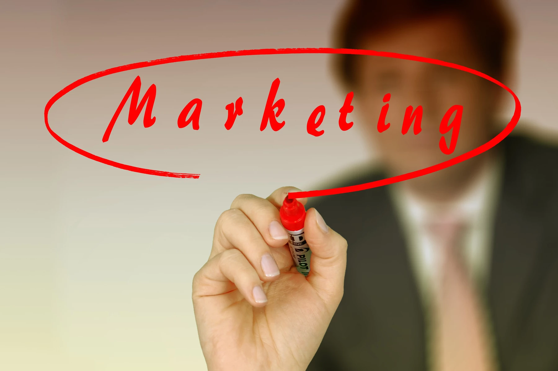 A man in a suit writing "marketing" on a clear screen in bold red pen