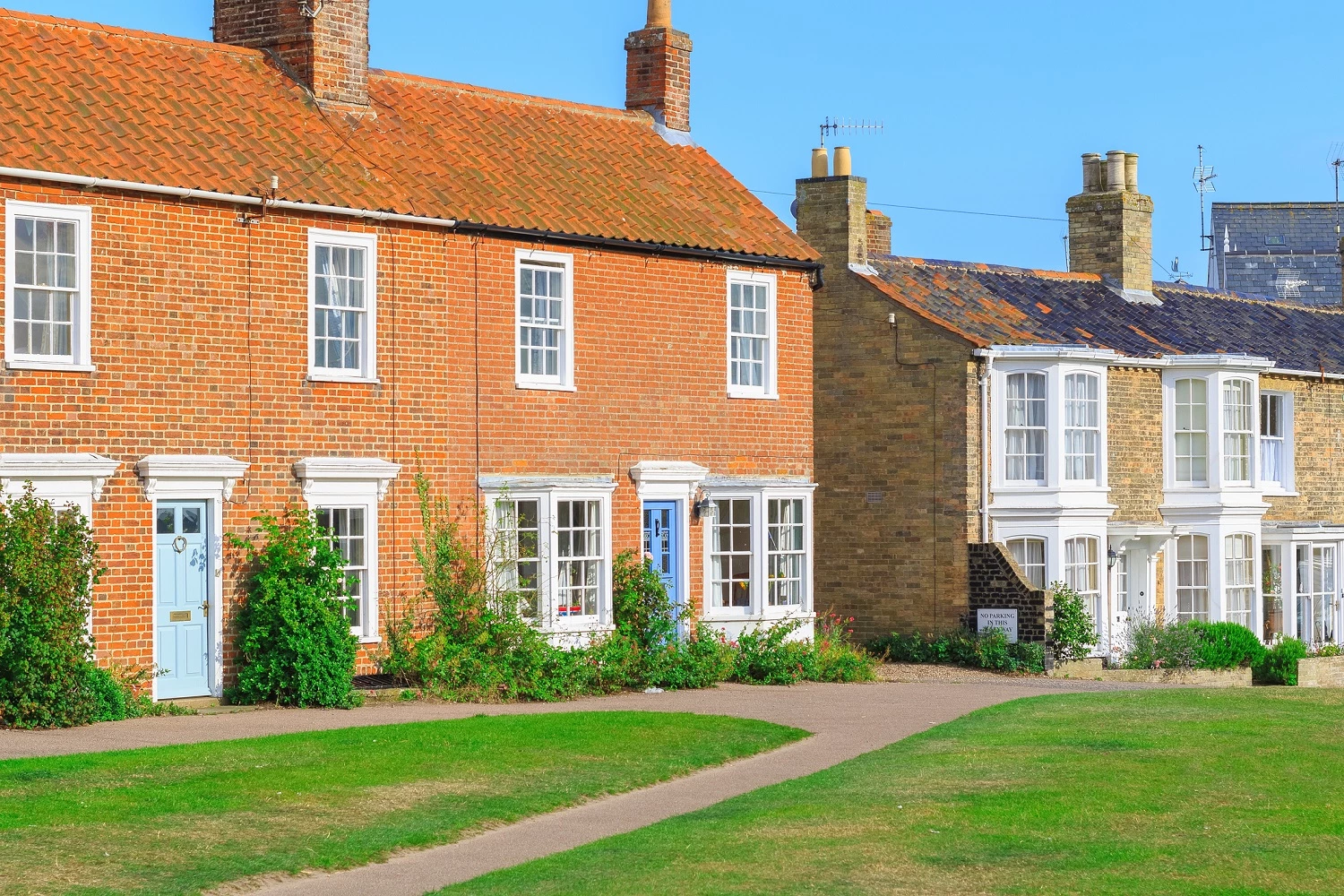 A semi-detached holiday home with a small grass lawn in-front on a sunny day