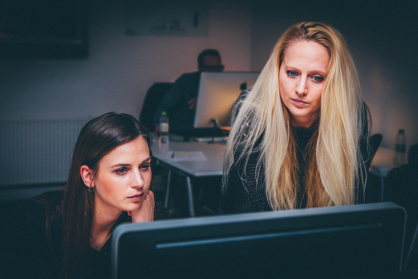 A more senior office worker showing a new starter something on a computer screen