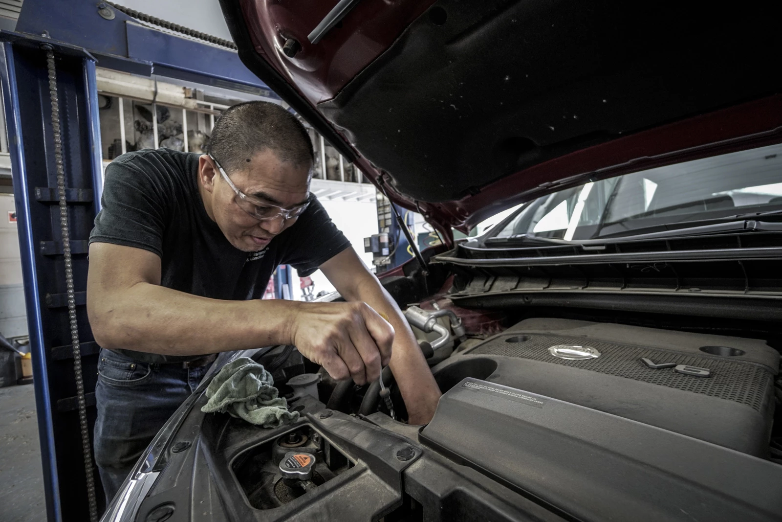 A technician leaning over an engine bay working on the car
