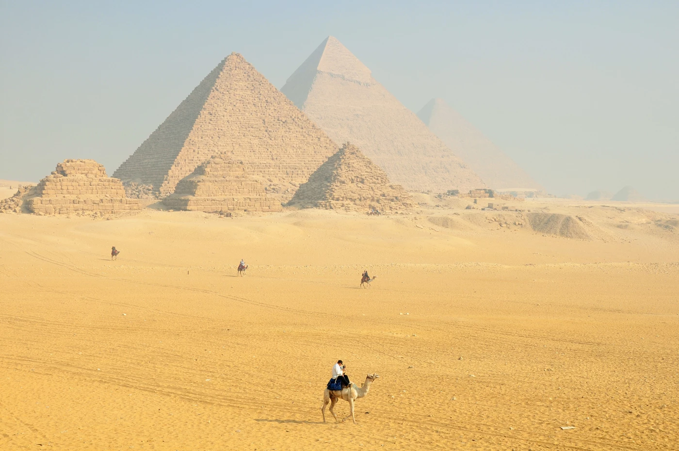 The Pyramids of Giza in the distance with a man on a camel walking across the desert towards them 