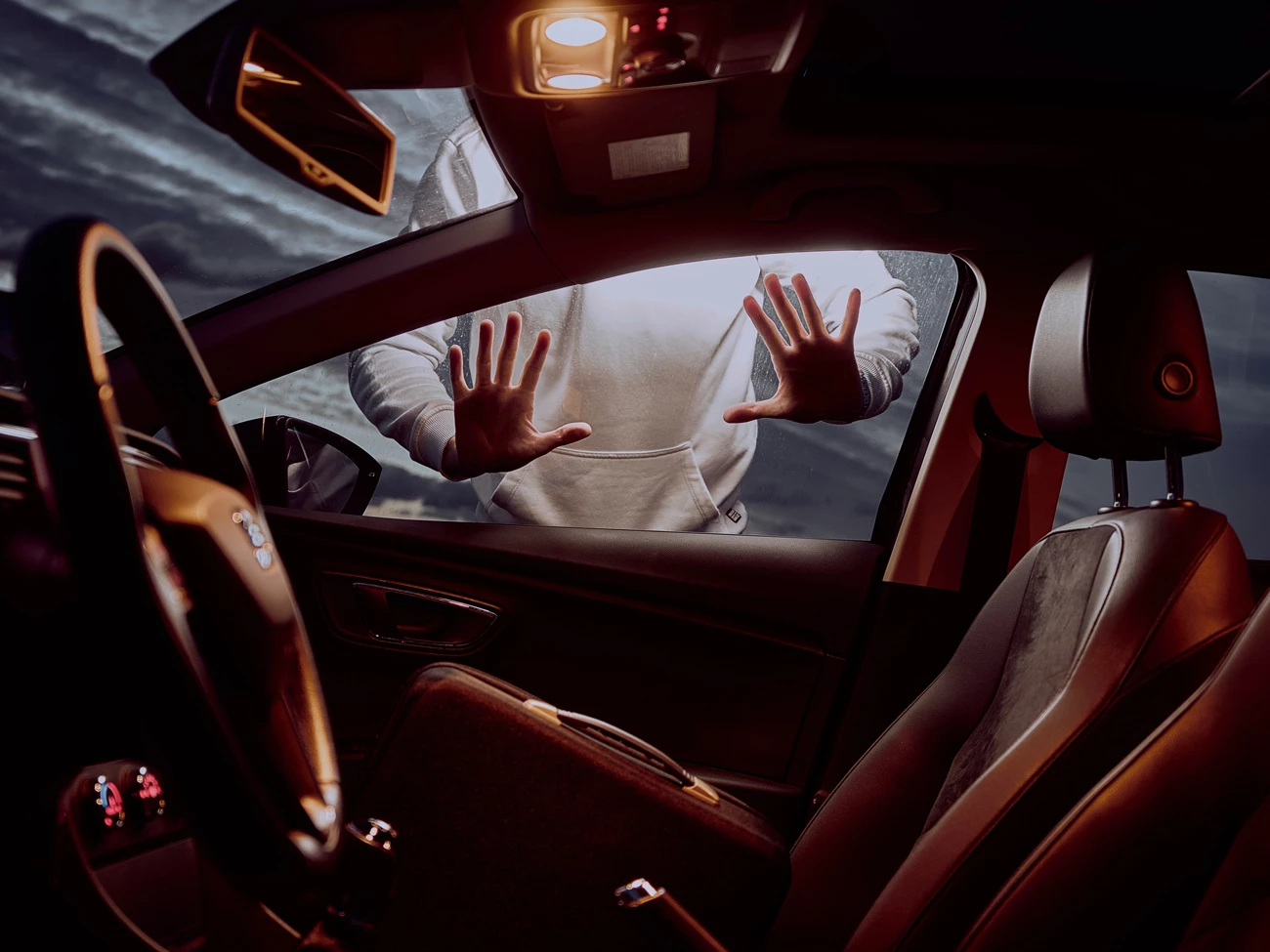 A car thief putting their hands on the window of a parked car