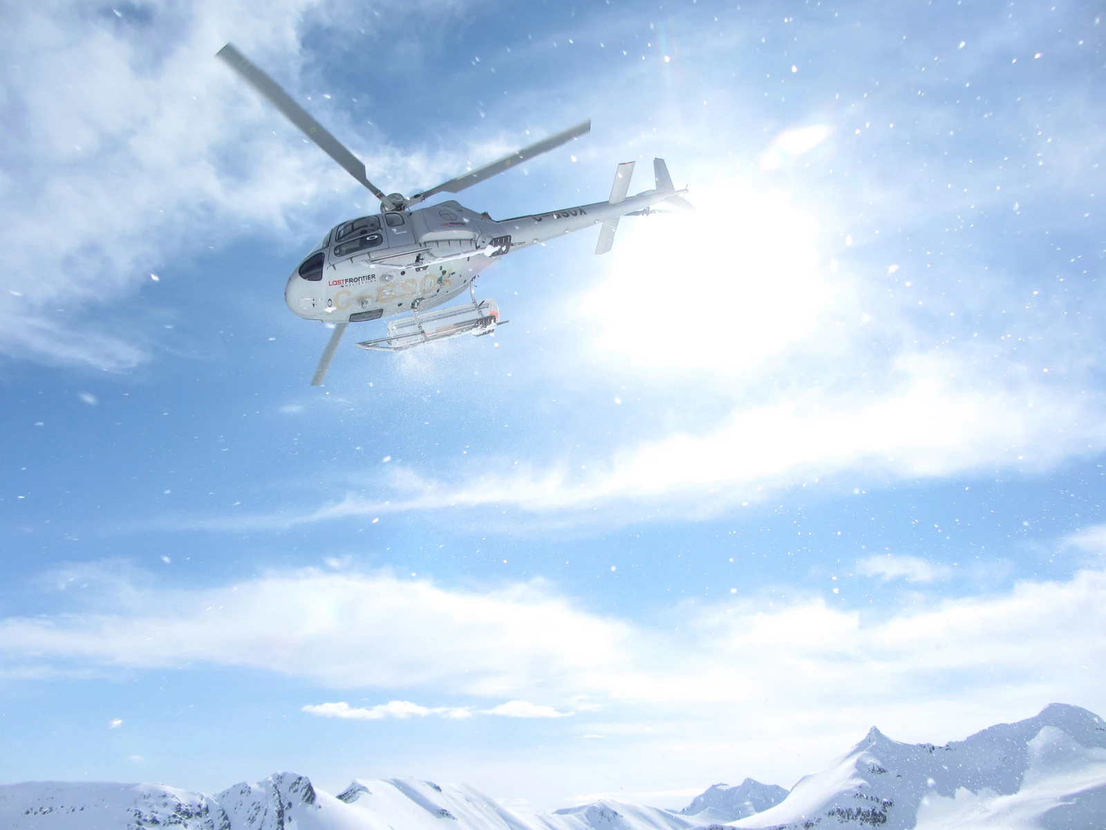A helicopter flying overhead in snowy conditions on a sunny day