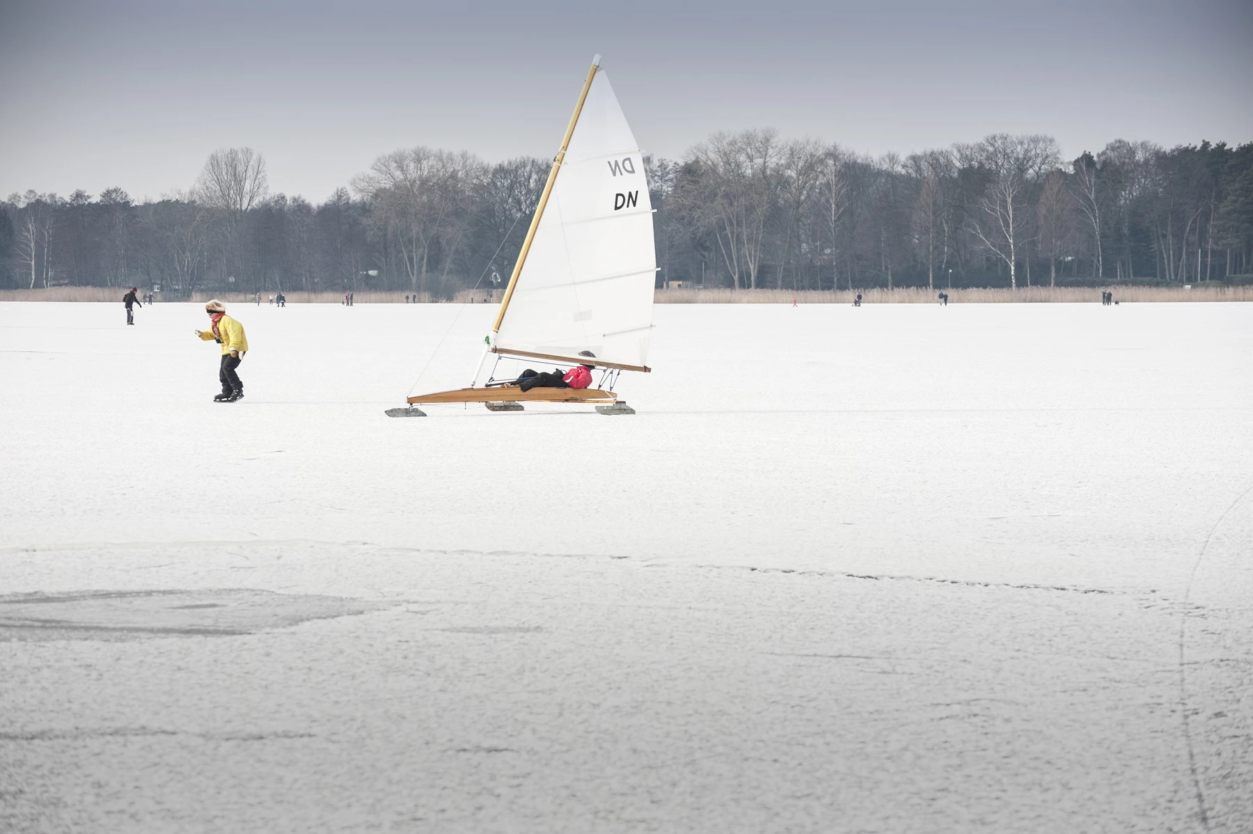 A person ice yachting on a frozen lake with other people ice skating