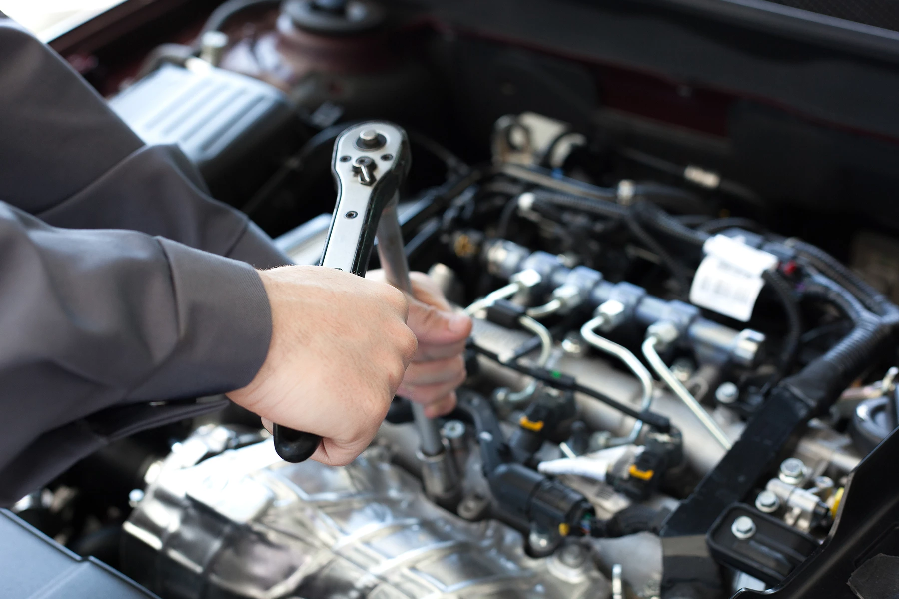 A mechanic using a ratchet to undo a bolt on a car engine in a motor repair garage